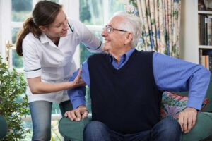Two older adults chatting over tea at a small shared dining table in a sunny common room.